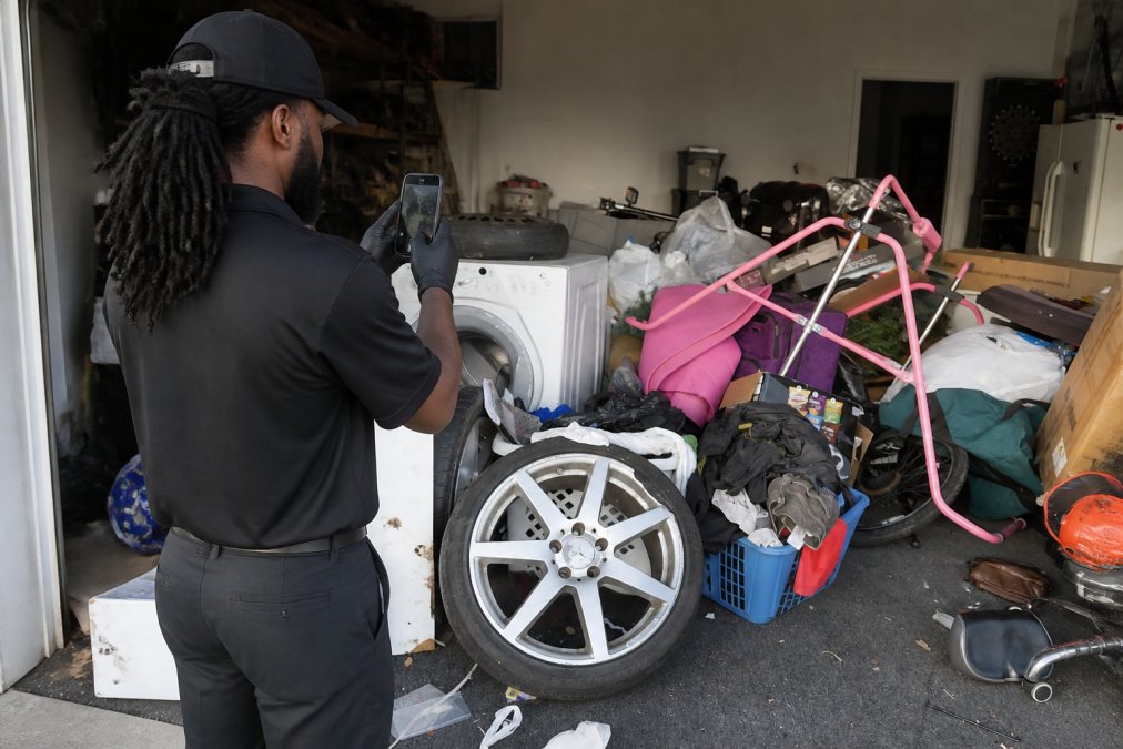 Professional junk removal team member photographing items in garage and basement, assessing volume and condition for on-site estimate, natural lighting