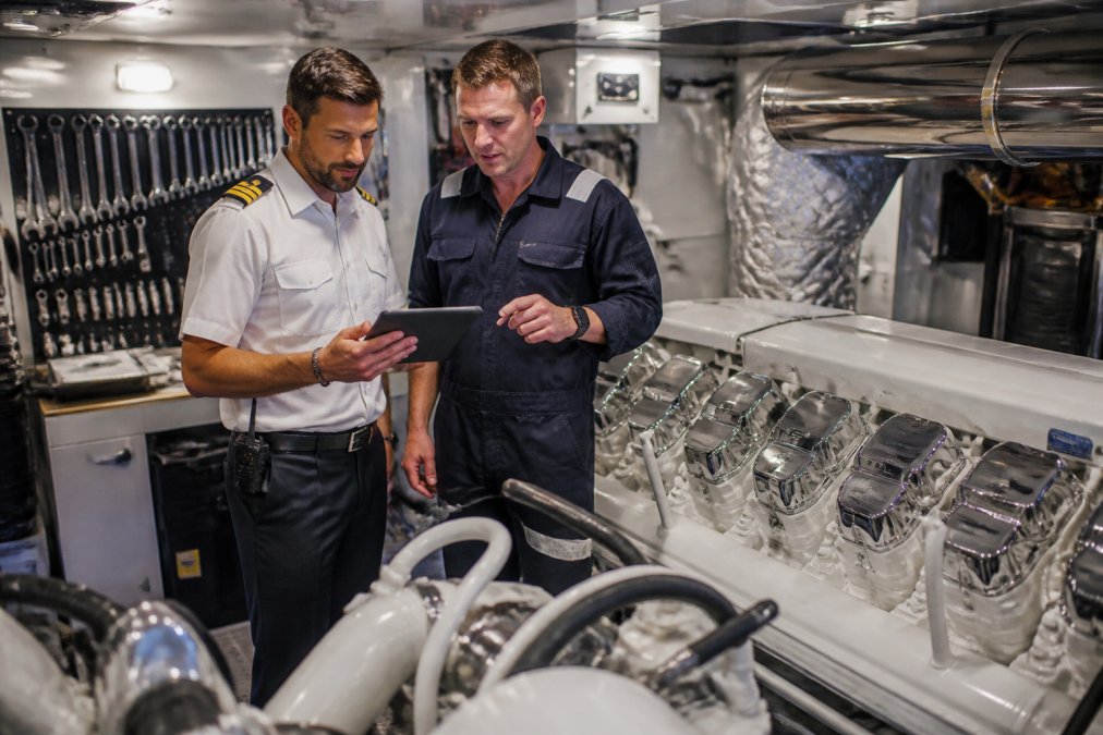 Captain and engineer reviewing the cost of maintaining a 50m yacht on a tablet in a luxury engine room.