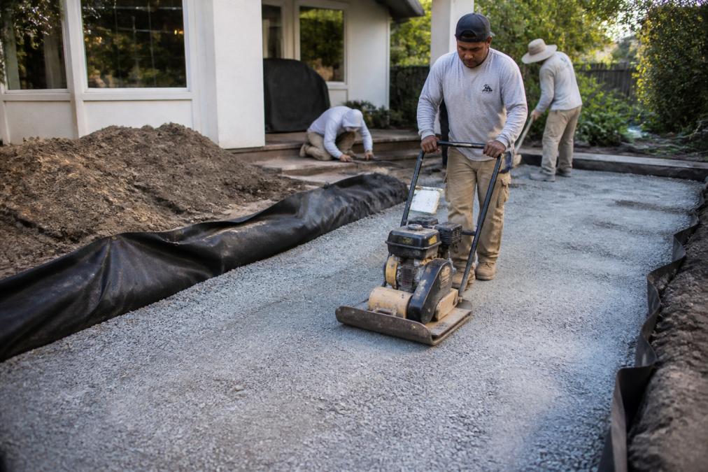 Cost of Paver Patio Installation 2026: Complete Price Guide 2 Hardscape crew compacting a crushed stone sub-base for the cost of paver patio installation 2026 project.
