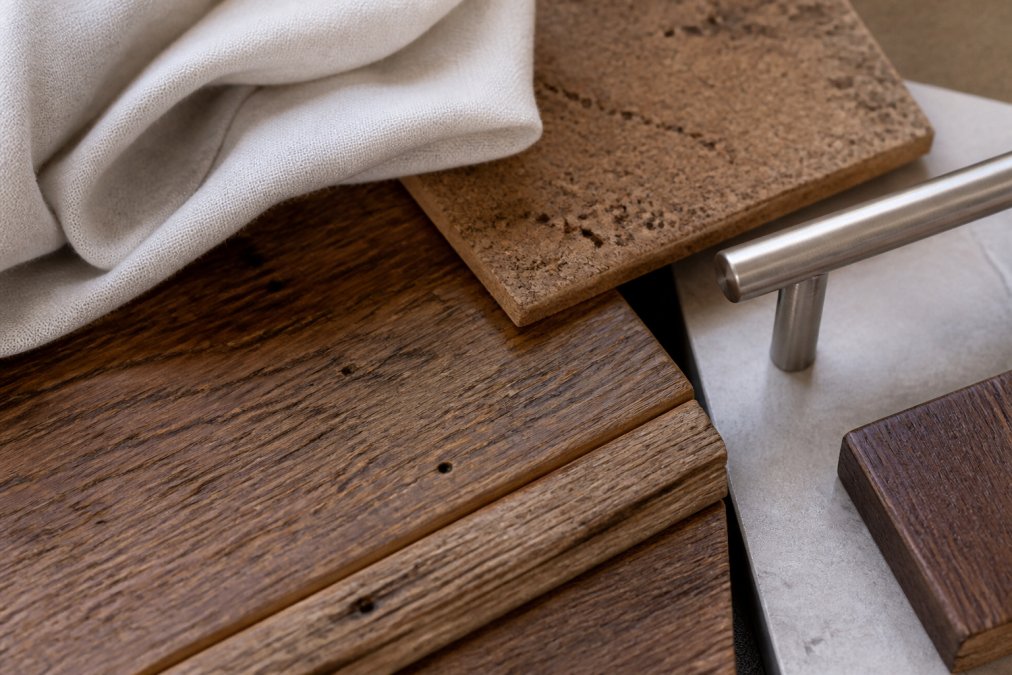 Close-up of natural sustainable materials arranged together, rich reclaimed wood grain, organic linen textile in cream, cork texture, and brushed metal accents, showing the tactile quality and earthy color palette that defines sustainable home decor