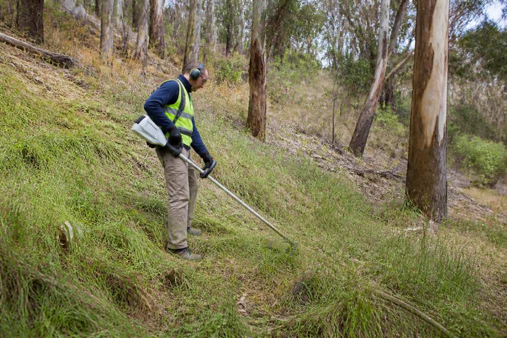 Worker using a brush-cutter on a steep slope to meet grass height regulations
