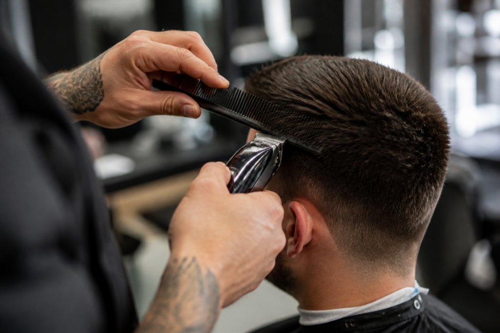Close-up of barber's hands holding comb at precise angle while using clipper on hair plateau, showing sectioning technique and cutting precision