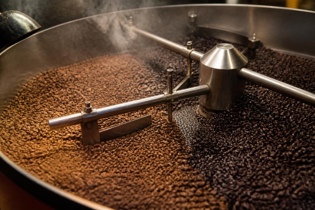Close-up of freshly roasted coffee beans cooling on a roasting table with steam rising, showing the progression from light golden to deep chocolate brown tones