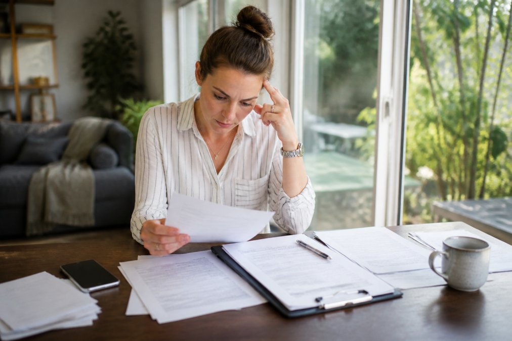 Person reviewing accident documentation and insurance paperwork at desk with laptop, phone, and printed forms, natural window lighting, focused expression