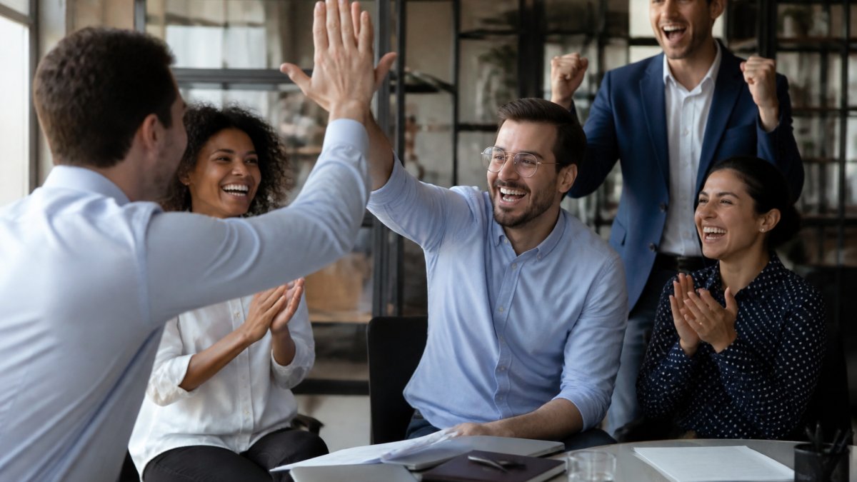 Sales team members celebrating and high-fiving in a modern office after closing a deal, showing genuine excitement and camaraderie