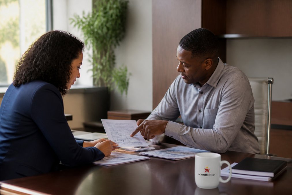 Professional financial advisor meeting with a client at a desk, reviewing credit report documents and financial statements in a modern office with natural lighting