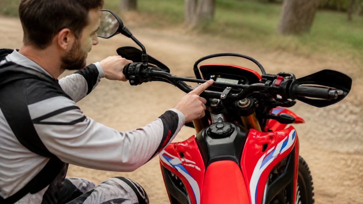 Rider in protective gear performing pre-ride checks on a Honda CRF300L motorcycle, examining the dashboard warning lights and fuel gauge in natural daylight
