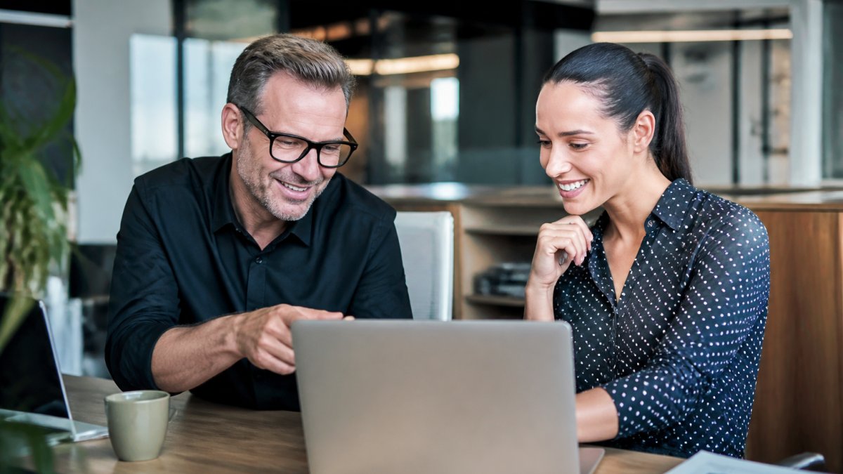 CRM Customer Relationship Management Software Guide A small business owner and a marketing specialist reviewing customer data on a laptop in a bright, modern office, pointing at the screen and smiling