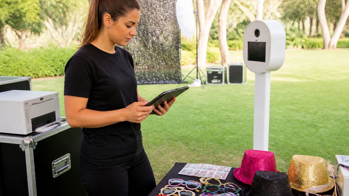 Photo booth operator reviewing event bookings on a tablet during an outdoor equipment setup