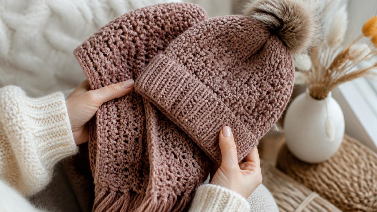 Close-up of hands holding a handmade crochet beanie and matching scarf set, showing intricate stitch detail and soft texture, with warm winter lighting