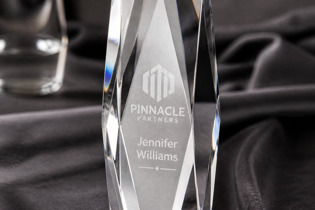 Close-up of intricately engraved crystal award surface showing laser-etched company logo and employee name with light reflecting through the crystal facets, highlighting the frosted engraving detail