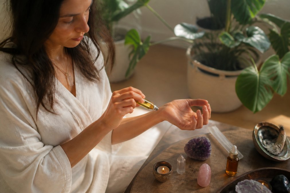 Person applying crystal infused oils for emotional healing from a roller bottle to their wrist in a serene room