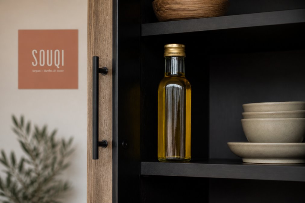 Glazen fles culinaire arganolie in een donkere keukenkast met gesloten dop, op neutrale achtergrond