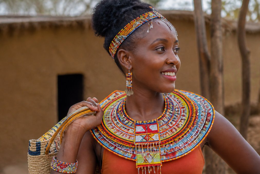 A woman of East African descent wearing traditional handcrafted beaded jewelry and woven accessories in natural daylight, styled authentically to show how cultural pieces carry meaning and craftsmanship