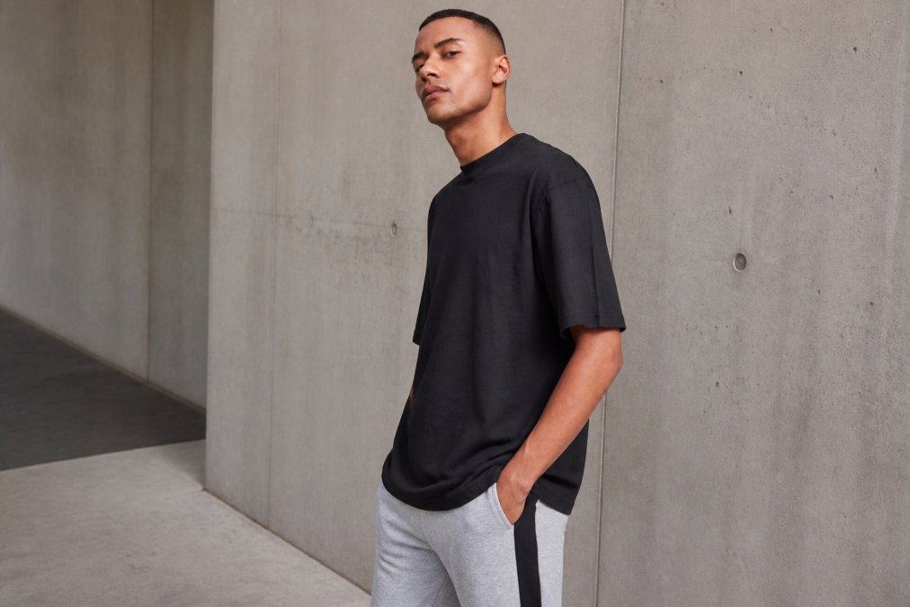Person wearing oversized black tee and tall tee from Urban Classics styled casually with neutral tones, showing fit and silhouette in natural daylight