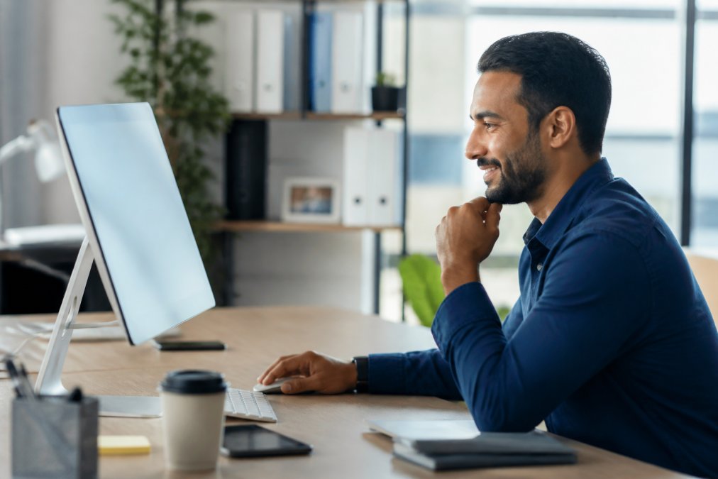 Small business owner reviewing analytics and automation workflows on a desktop computer in a modern office, looking focused and satisfied with results displayed on screen