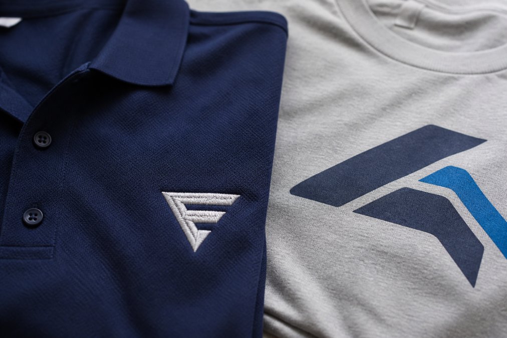 Close-up of a polo shirt with embroidered corporate logo next to a t-shirt with screen-printed design, showing detail and texture differences in the embroidery and print