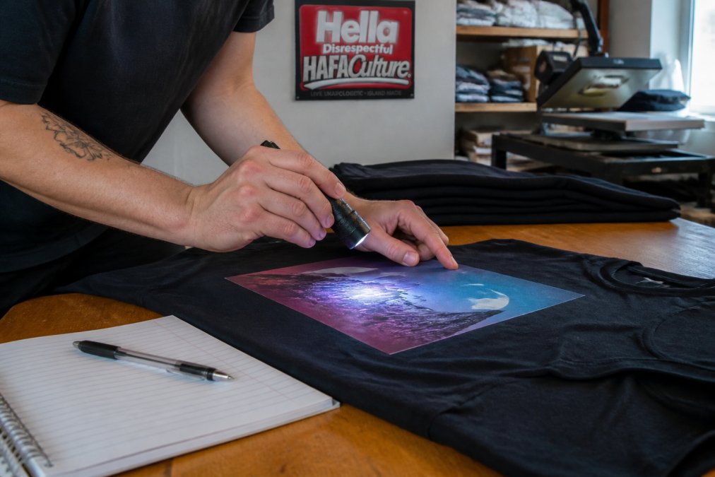 Hands inspecting DTF-printed t-shirt edges and colors as part of custom apparel quality control steps