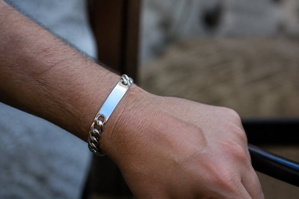Close-up of a man's wrist wearing a sterling silver ID link bracelet with visible engraved nameplate, showing the chain detail and polished silver shine under natural light