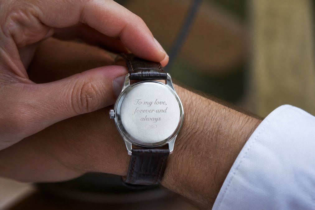Close-up of a man's wrist wearing an elegant engraved watch, with soft natural lighting highlighting the dial and personalized caseback detail, showing the custom inscription on the back