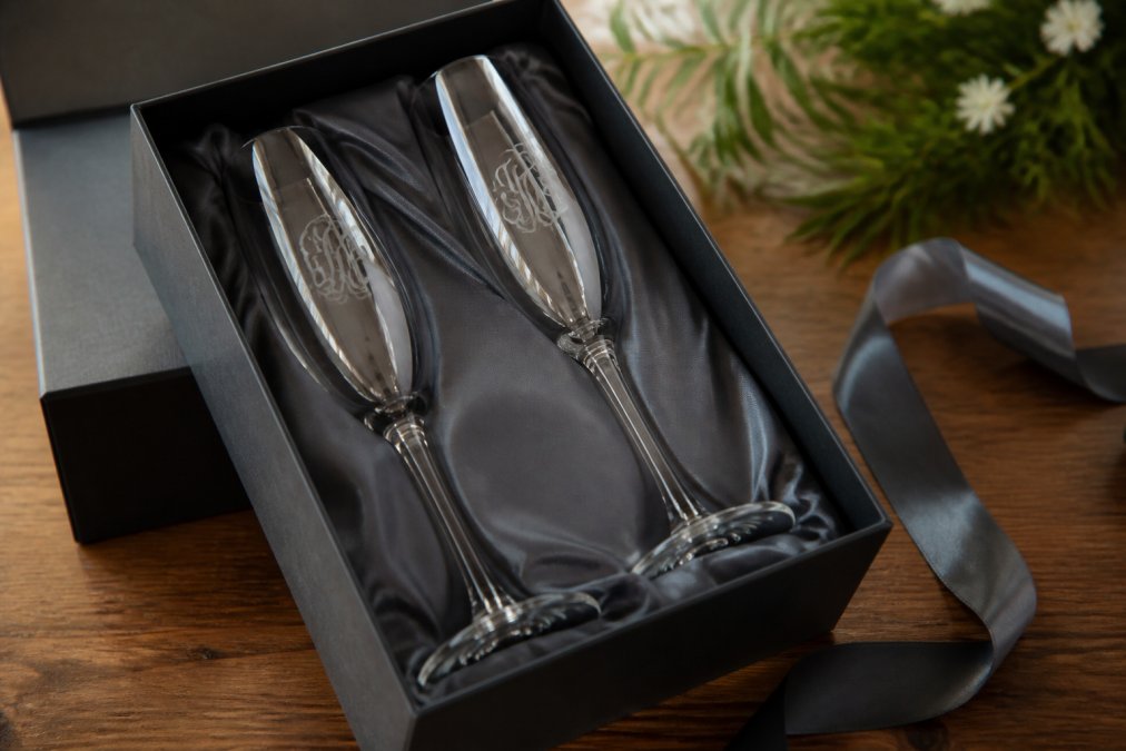 Two elegant etched champagne flutes with custom monograms displayed in a premium fabric-lined gift box.