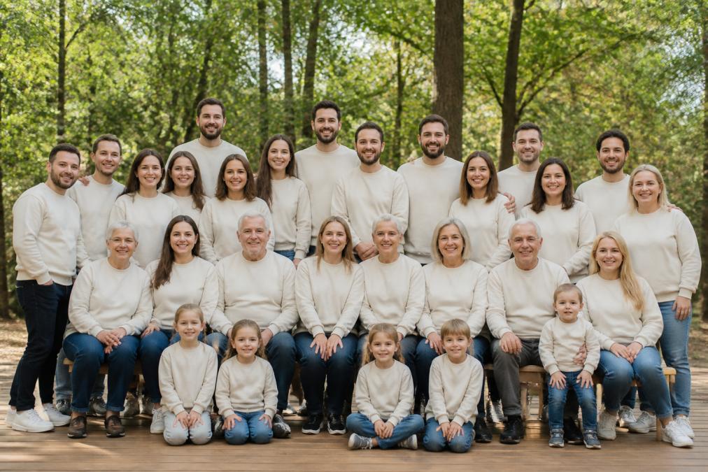 A multi-generational family arranged for a formal group photo, all wearing coordinated custom sweatshirts with personalized family name and 2026 reunion text, demonstrating matching apparel across different body types, ages, and sizes in natural outdoor lighting