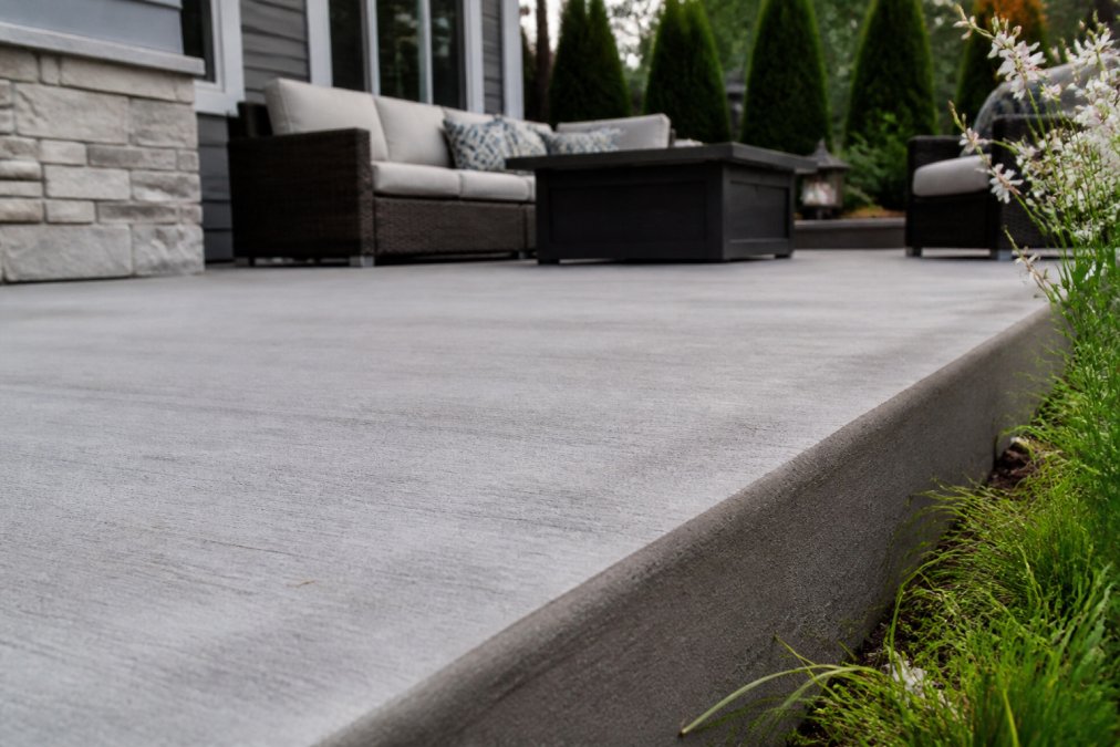 Close-up of a finished concrete patio surface showing smooth texture and clean edges, with outdoor furniture and landscaping visible in the background