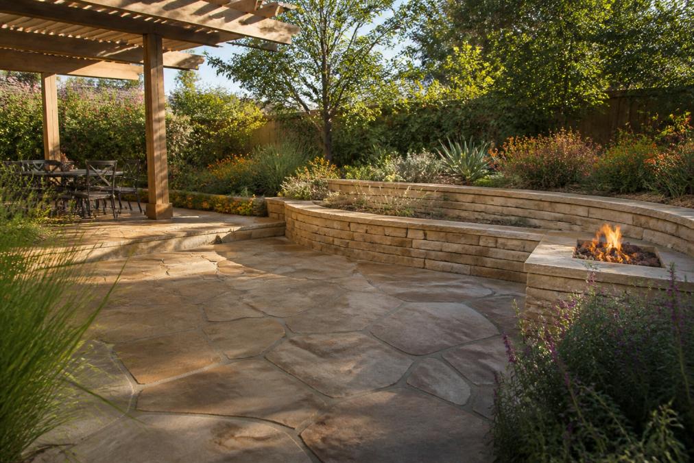 Flagstone patio with a stone seating wall and fire feature creating a cozy outdoor living space under a pergola.