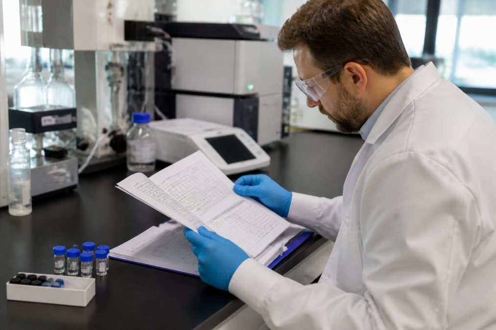 Professional researcher examining laboratory test results and documentation papers at a workbench with peptide vials and analytical equipment visible in modern laboratory setting