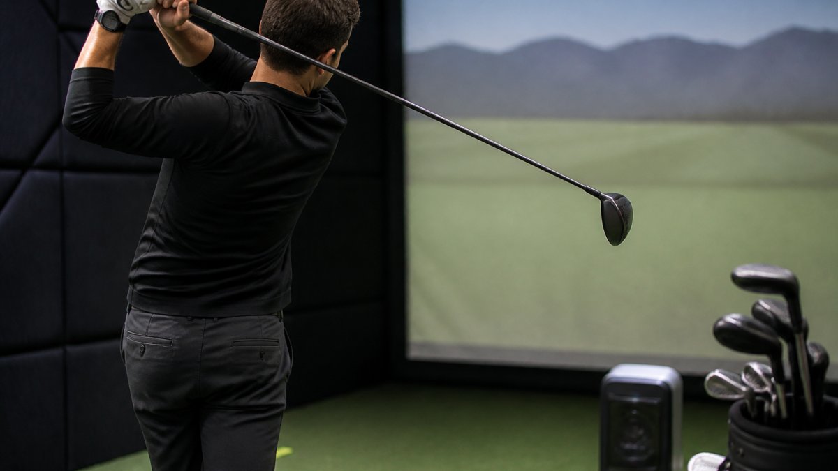 Professional golfer demonstrating swing with launch monitor display visible in background, showing shaft flex and weight characteristics during impact