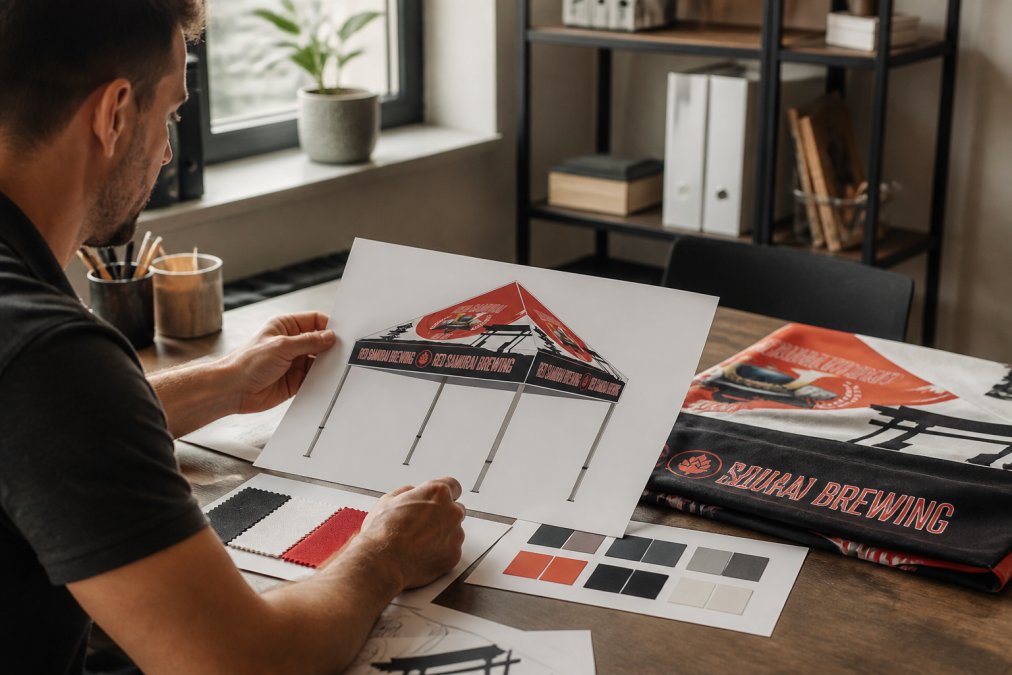 Designer or business owner reviewing custom signage mockups and brand guidelines on a desk with color swatches, fabric samples, and design sketches nearby in natural office lighting