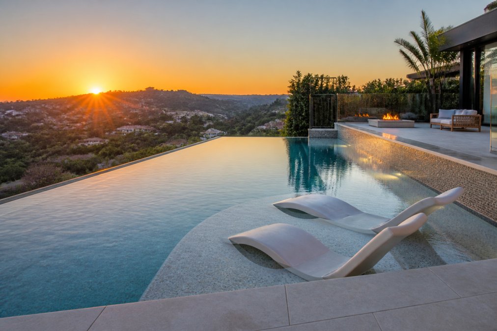 Modern geometric infinity pool with glass tiles and a baja shelf reflecting 2026 luxury pool design trends at sunset.