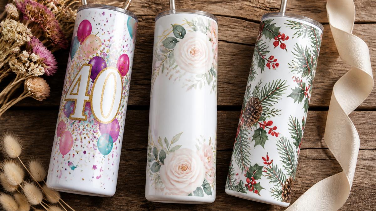 A flat-lay of three personalized 20 oz stainless steel skinny tumblers on a rustic wooden table, each with a different occasion theme: one with birthday confetti and a milestone number, one with delicate floral wedding artwork and a date, and one with a holiday motif, styled with ribbon and dried flowers nearby