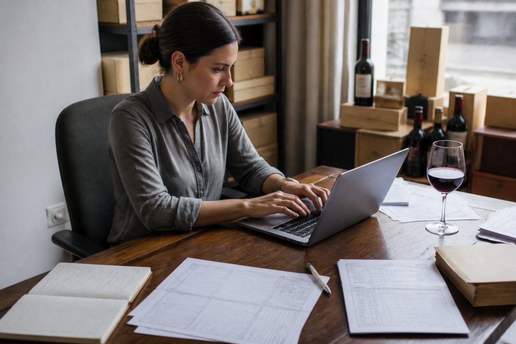 Wine importer working on customs duties paperwork on a laptop at a desk