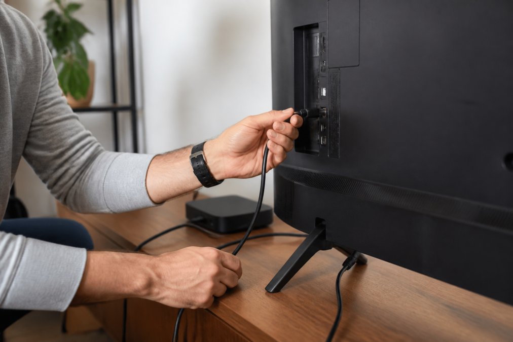 Close-up of hands connecting Superbox device to television with HDMI cable and power cord on an entertainment center, showing proper cable management