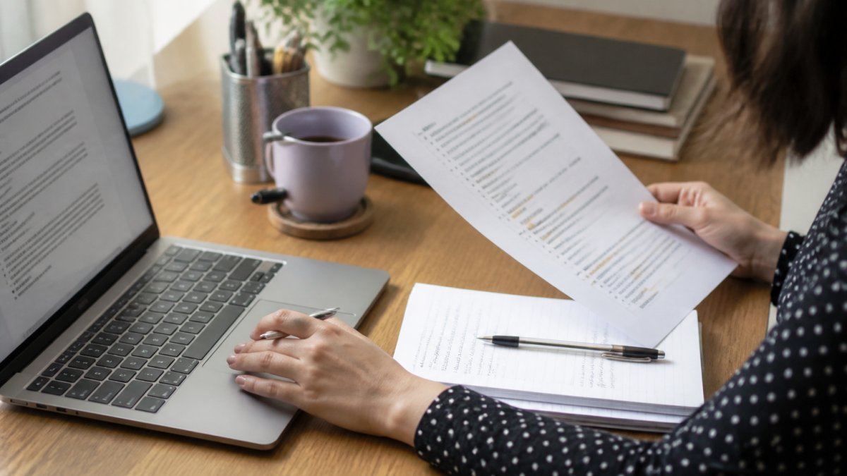 Professional reviewing and editing CV on laptop screen with notes and achievement highlights visible, focused on detail and precision