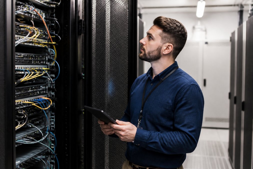 Security professional conducting a vulnerability assessment, examining network equipment and security systems in a hotel server room with focused lighting