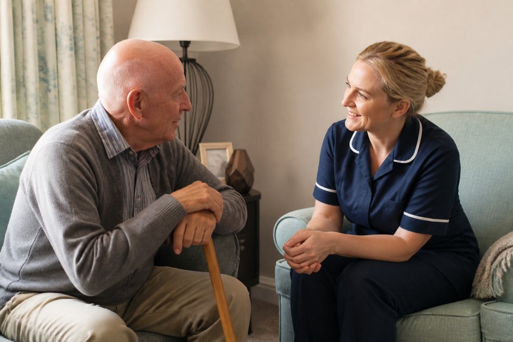 Professional caregiver having a warm, respectful conversation with an older adult in a comfortable home setting, building trust and rapport through attentive listening and genuine connection