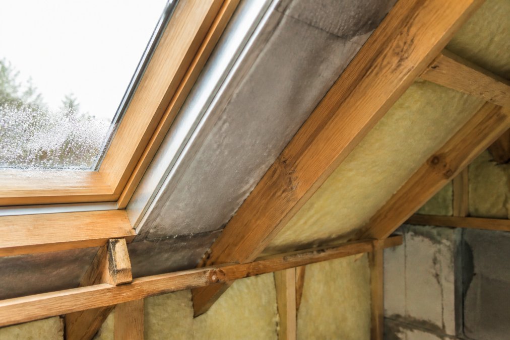 Close-up van isolatiemateriaal in dakopbouw met zichtbare vochtophoping en condensatie op binnenoppervlakken, natuurlijk daglicht
