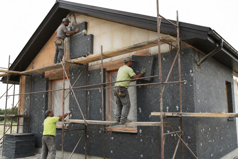 Bouwvakkers voeren gevelisolatie uit aan de buitenzijde van woning met steigers, isolatieplaten zichtbaar in verschillende stadia van installatie