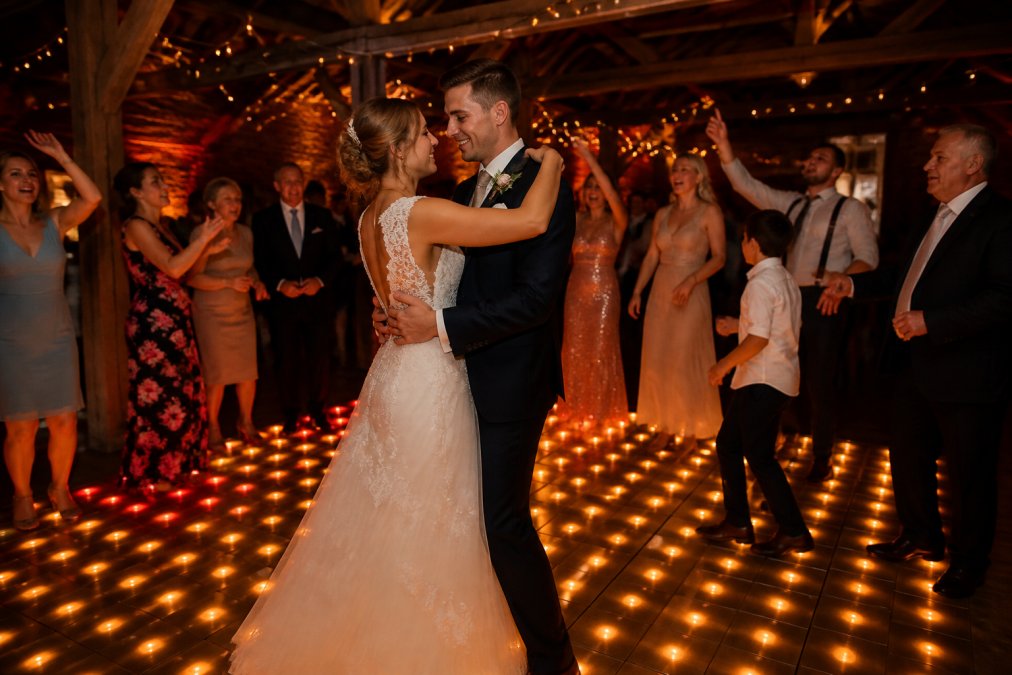 Bruidspaar dansend op verlichte LED dansvloer met warm gouden en rode lichteffecten, omringd door dansende gasten en familie, sfeervolle feestverlichting in achtergrond