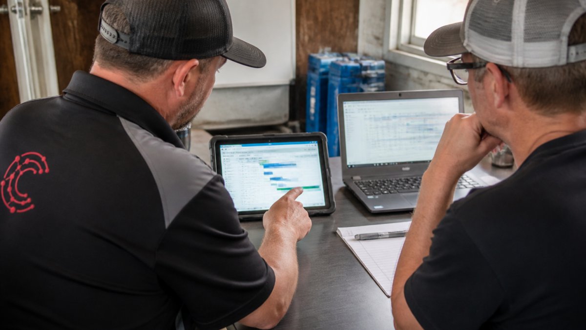 Restoration contractor team reviewing job details on a tablet and laptop in the field office, with job schedules and timesheets visible on screens
