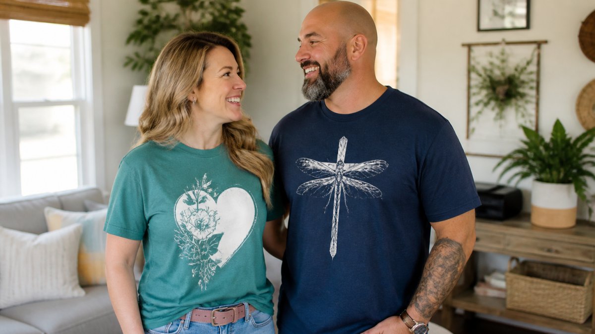A man and a woman wearing casual faith-inspired graphic tees, standing together in a bright, welcoming living room, warm natural light, relaxed and happy expressions