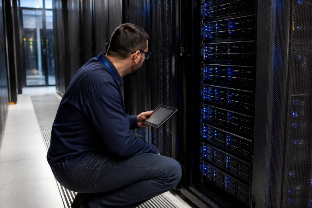Professional technician monitoring GPU server racks with blue LED indicators and control panels in a modern data center facility with cool ambient lighting