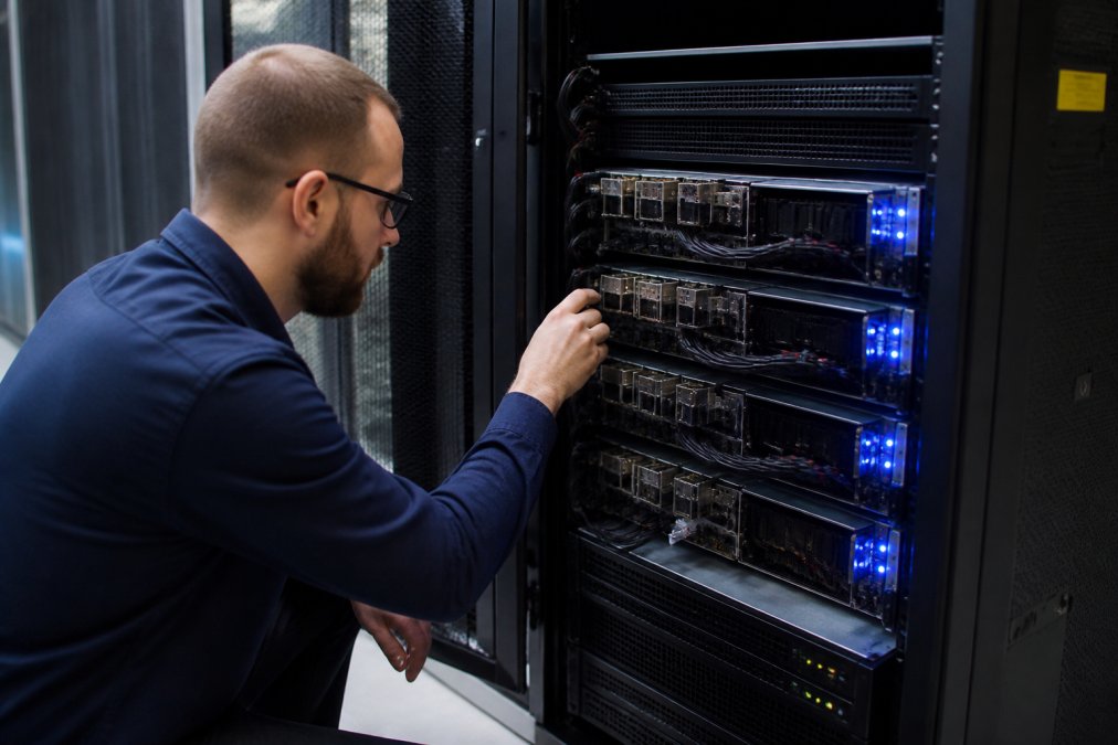 Technician inspecting a rack of dedicated gpu servers in a modern data center with blue status lights glowing