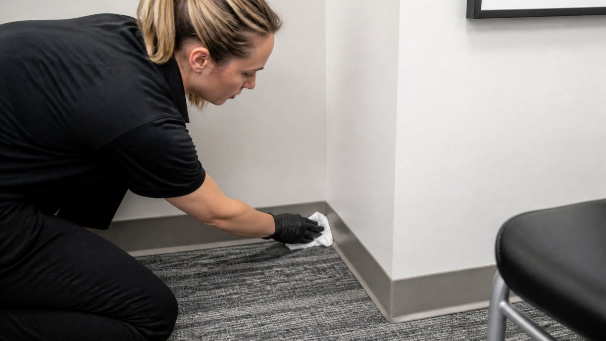 Close-up of a professional inspector checking baseboards and corners with a white cloth to verify deep-cleaning quality, showing attention to detail in a small office corner
