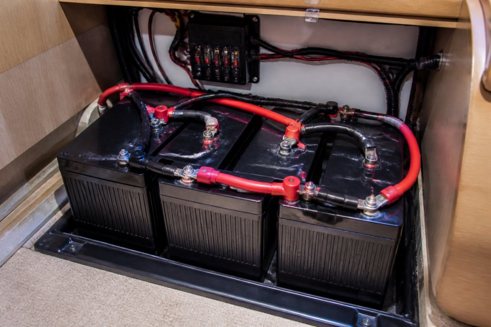 Installed marine battery bank secured in a boat cabin, showing multiple deep cycle batteries wired together with heavy-gauge cables and a battery management system display