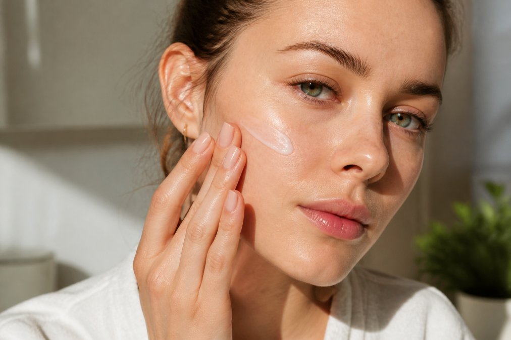 Nahaufnahme einer Hand, die eine leichte Gel-Creme-Feuchtigkeitspflege auf das Gesicht aufträgt, wobei natürliches Morgenlicht die Produkttextur und den Hautglanz hervorhebt