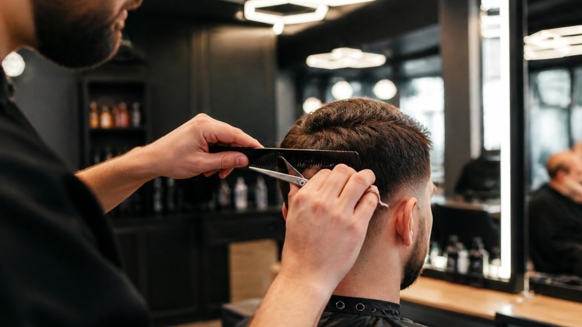 Un barbier réalise un dégradé de précision aux ciseaux et au peigne sur les cheveux d'un client en salon.
