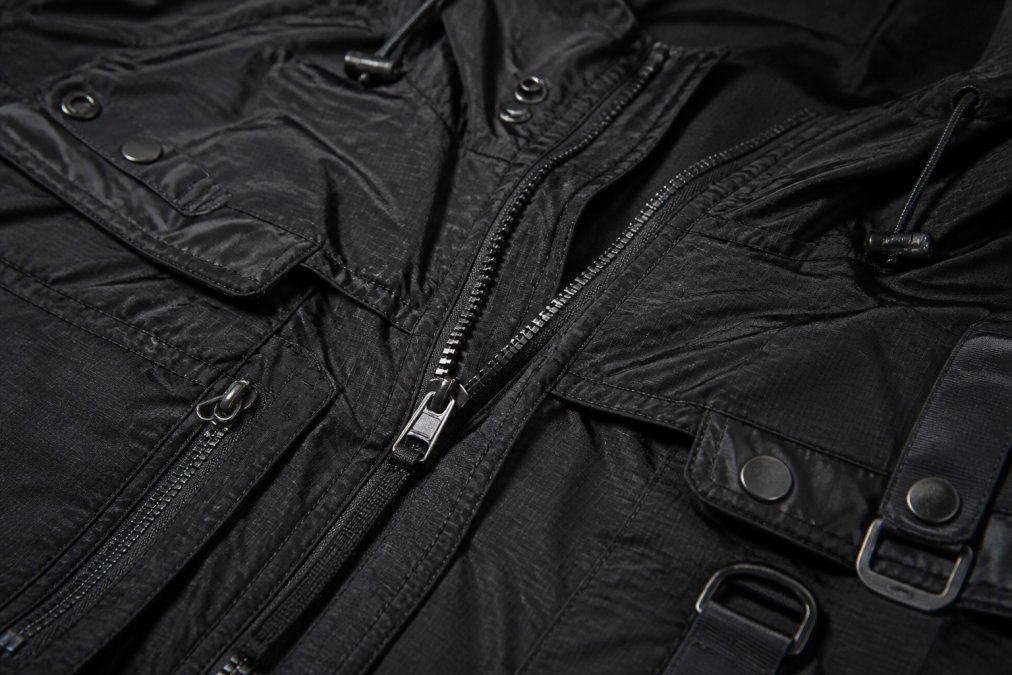 Detailed close-up of streetwear jacket hardware, metal zippers, reinforced seams, and utility snaps showing construction quality and material durability on dark technical fabric